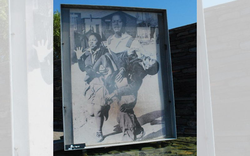 Photo of black and white picture of two young people. One of them is carrying a lifeless young body in his arms.